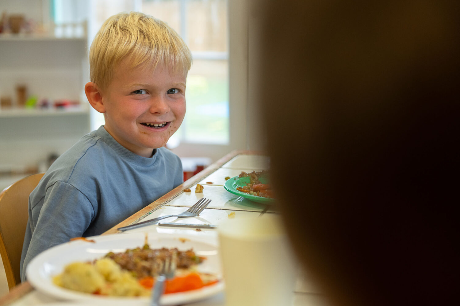 young boy smiling, eating his lunch