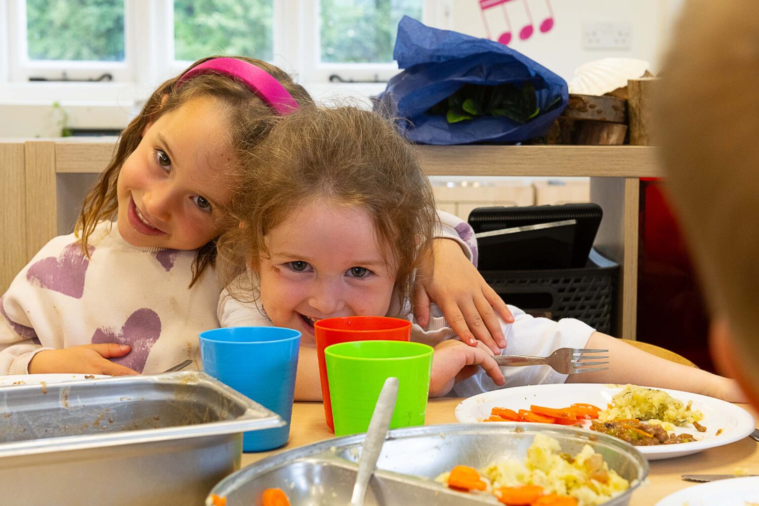 two girls hugging and smiling at the camera while eating lunch