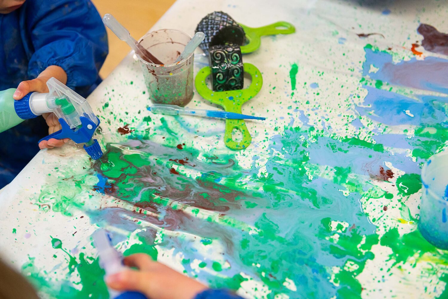 A table covered in paint splodges with paint rollers and pipets laid on the table