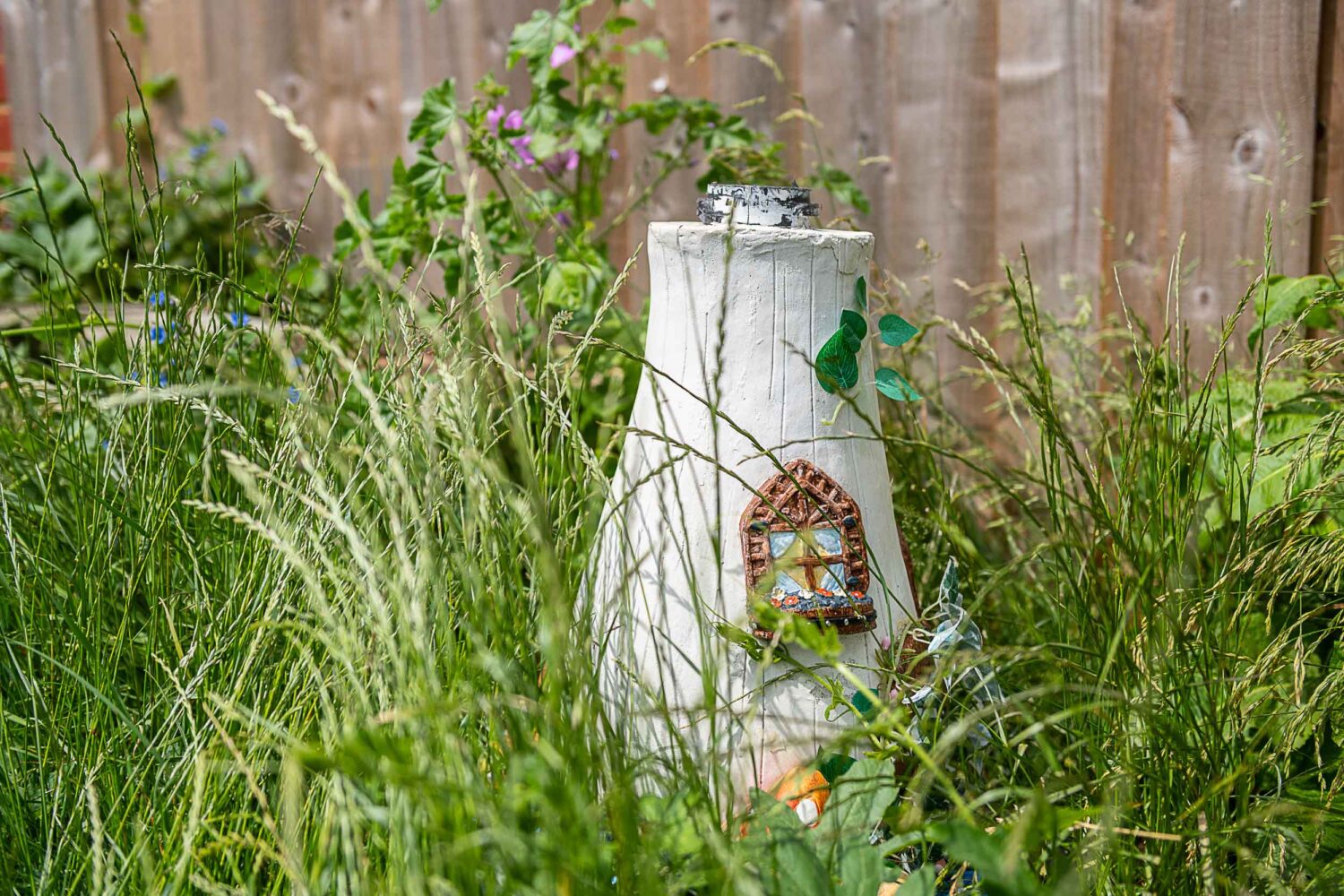 A small painted house placed buried in between wildy growing plants