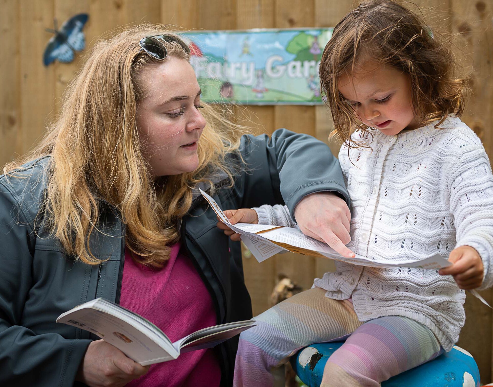 A member of staff helping a child read in the garden