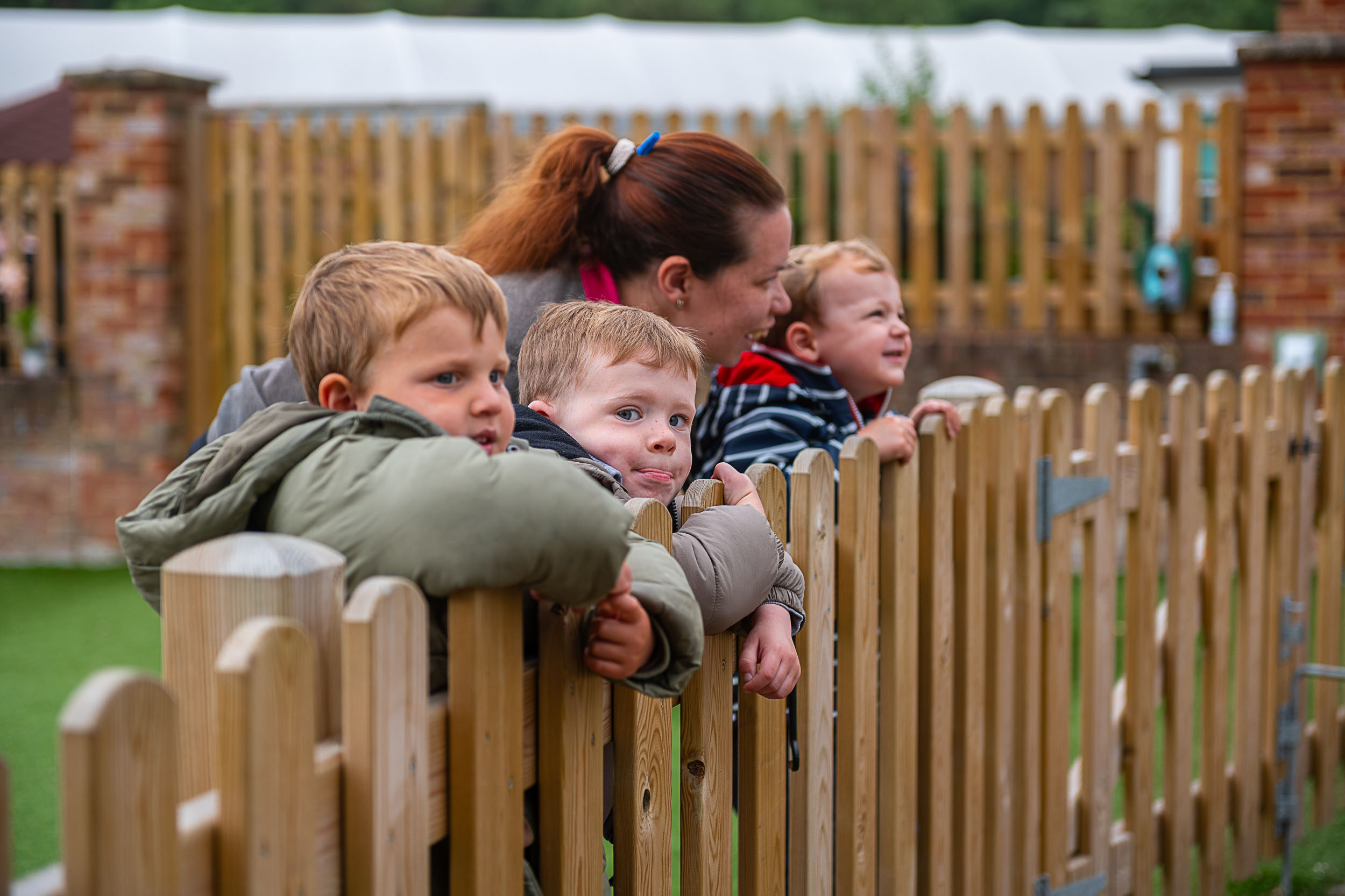 A group of young children with a staff member, looking over a fence