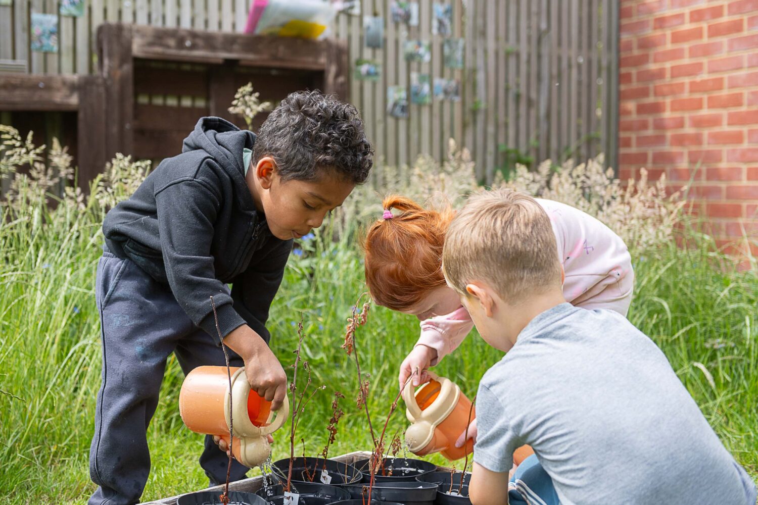 group of young children playing with toy watering cans, watering potted plants