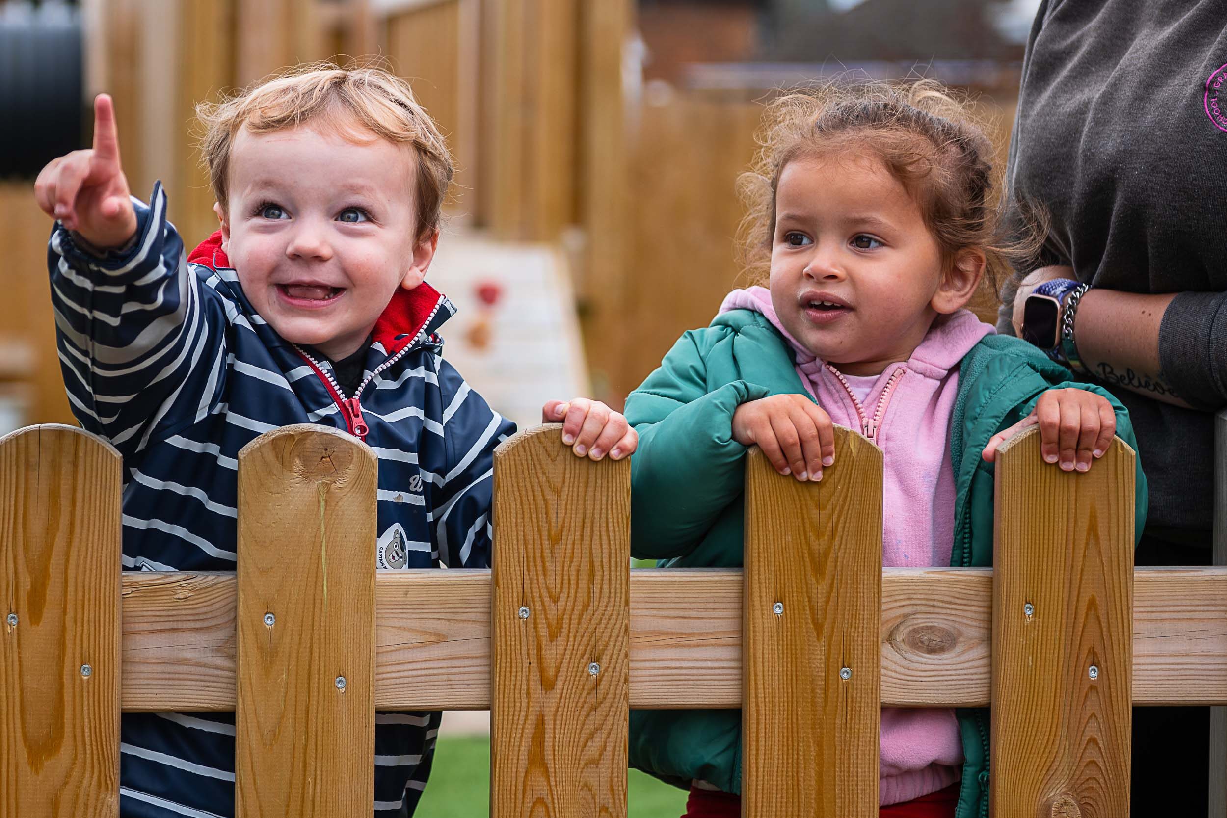 Two little kids smiling and point over a fence