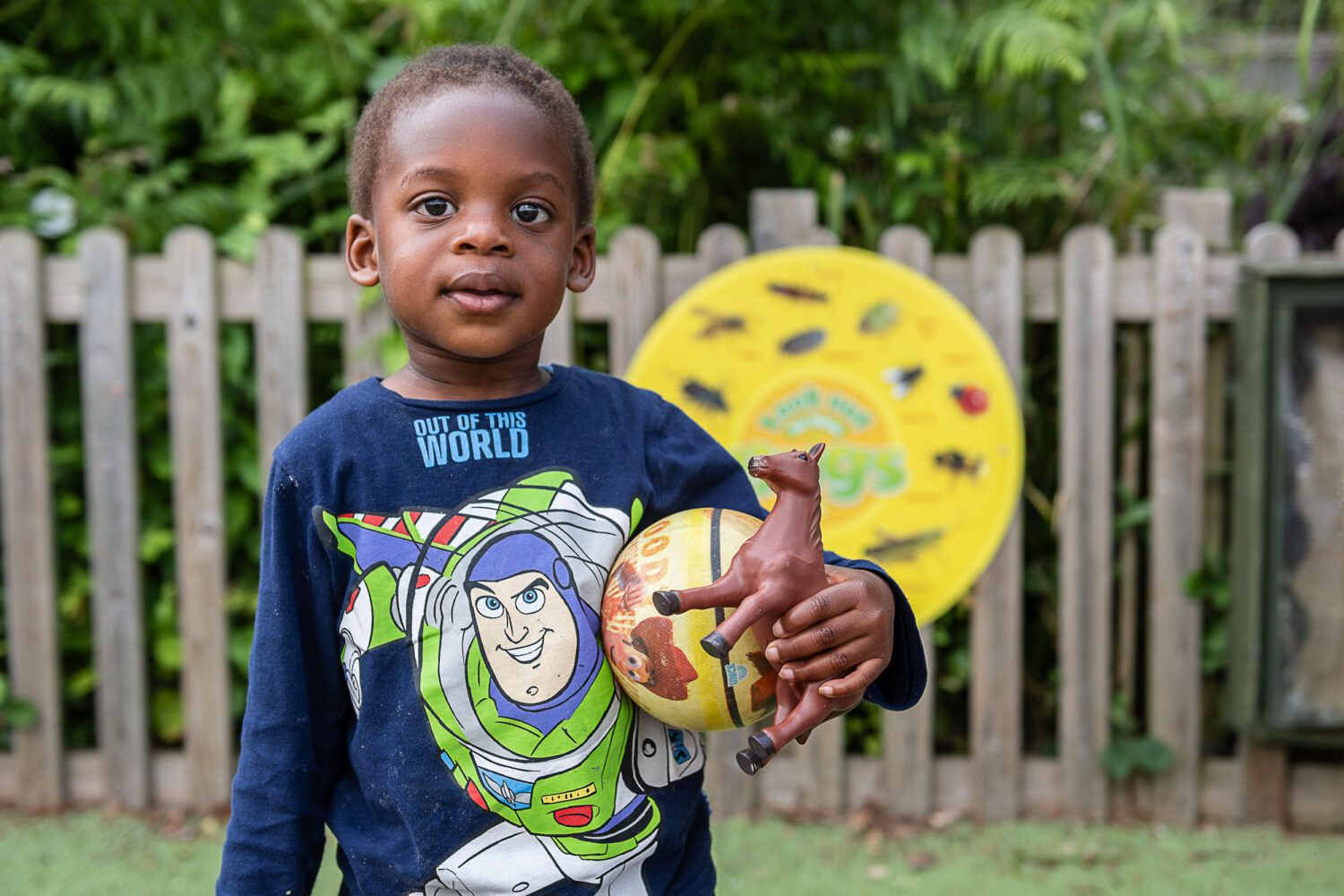 young boy looking at the camera holding a ball and toy horse