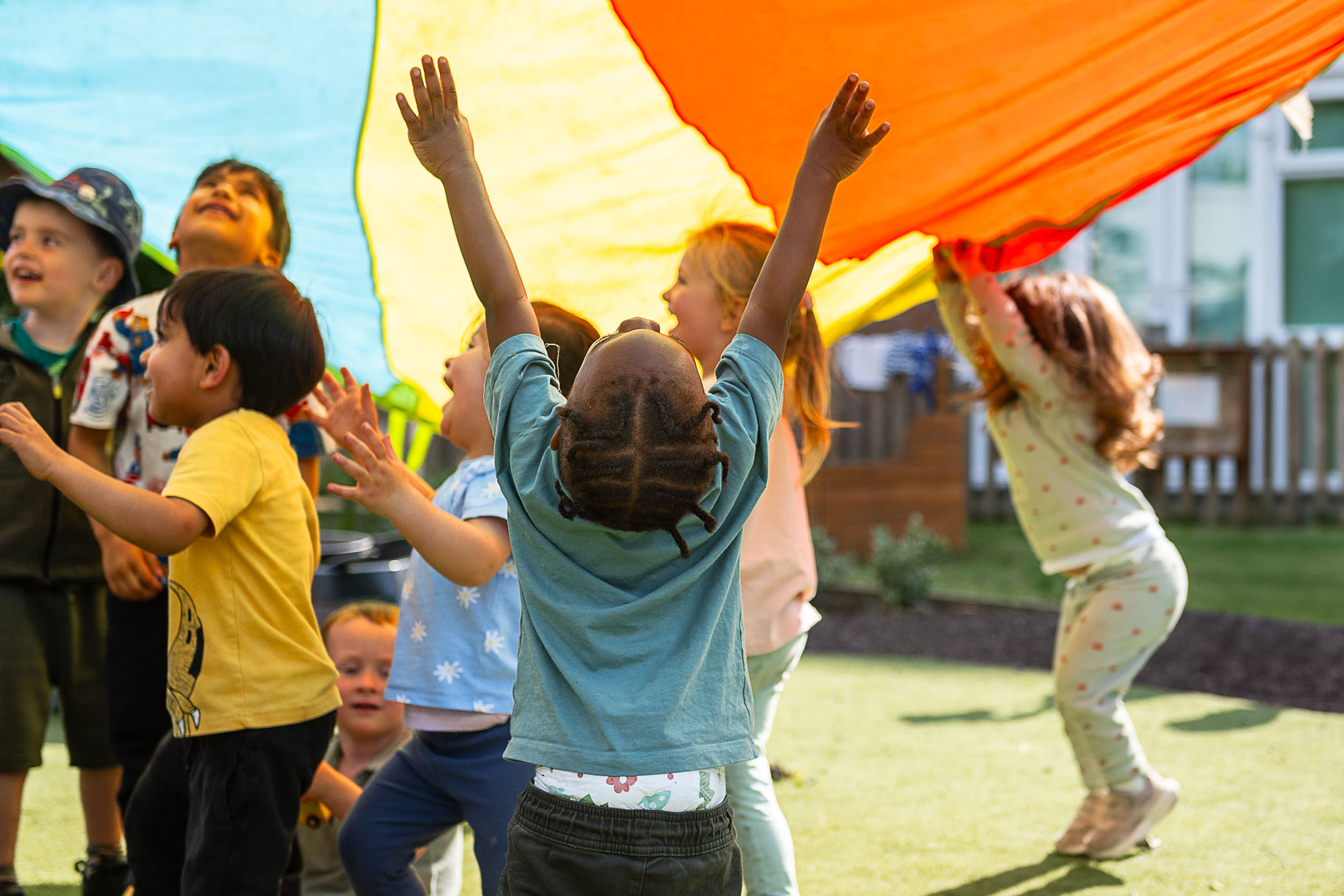 Children reaching and running under a large parachute