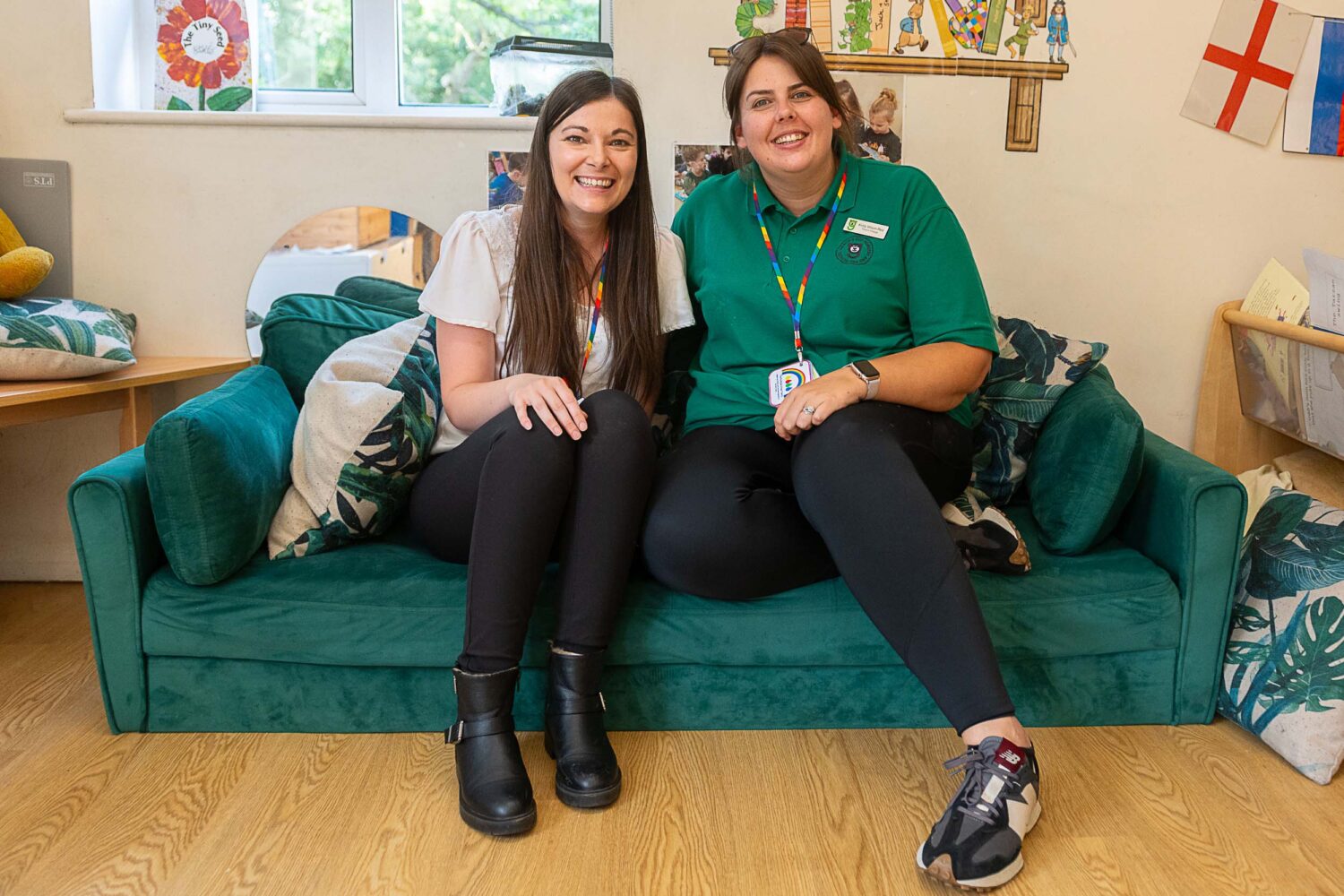 Two members of staff smiling at the camera, sat together on a sofa