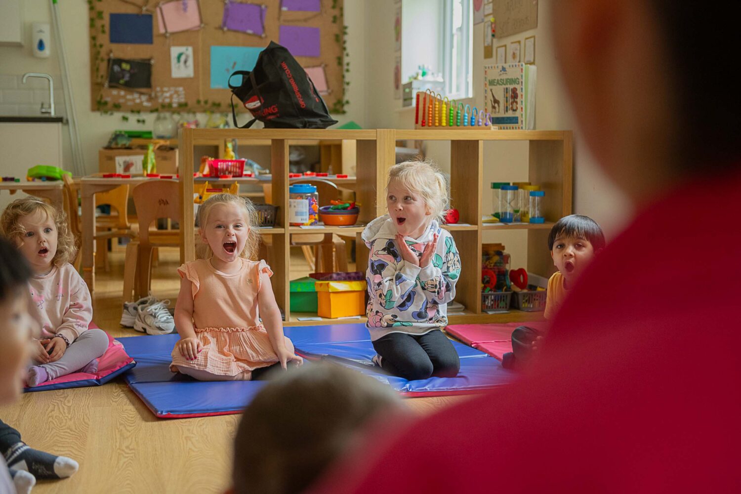 young girls sitting on play mats smiling and shouting at the member of staff