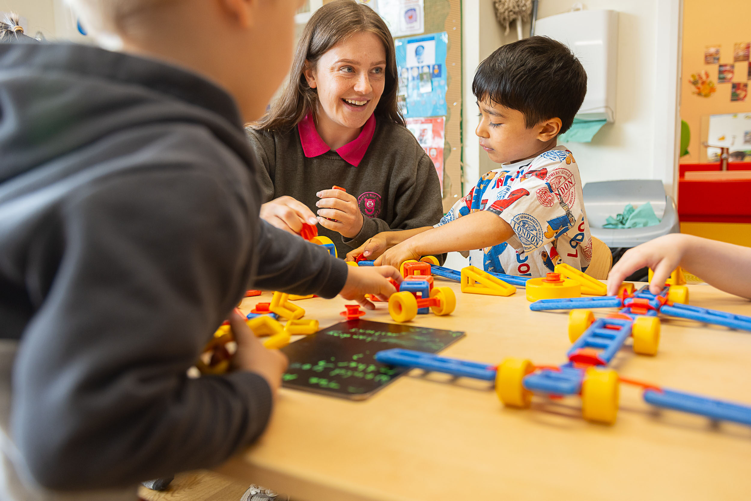 Staff member smiling, talking to the children while they play with toy bricks