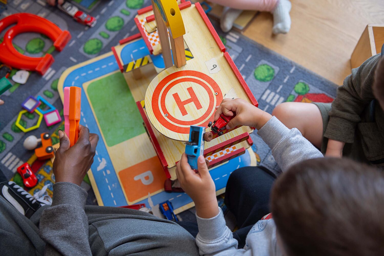 Children playing on a playmat with toy helipad and cars