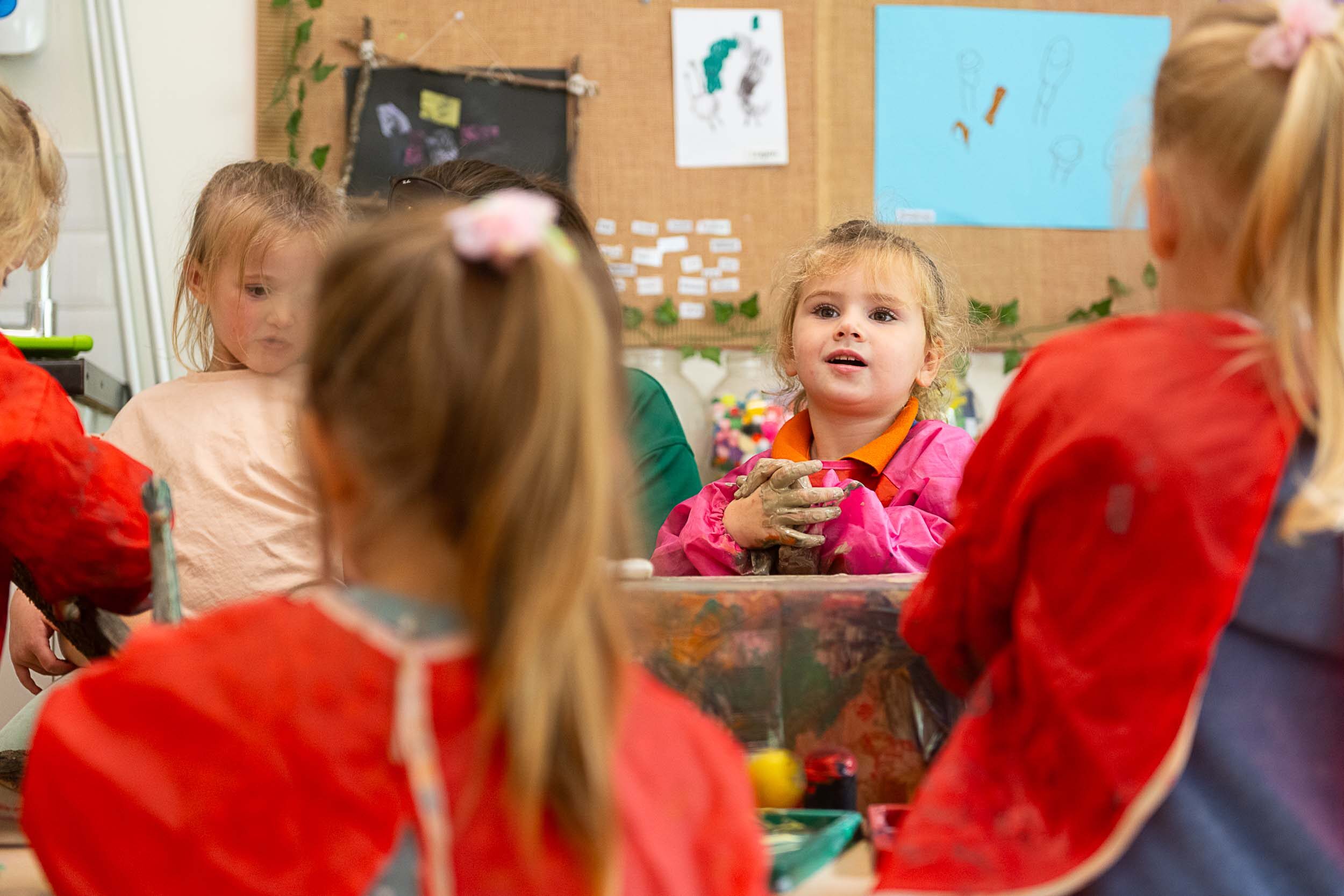 A group of little girls wearing aprons, painting on the table
