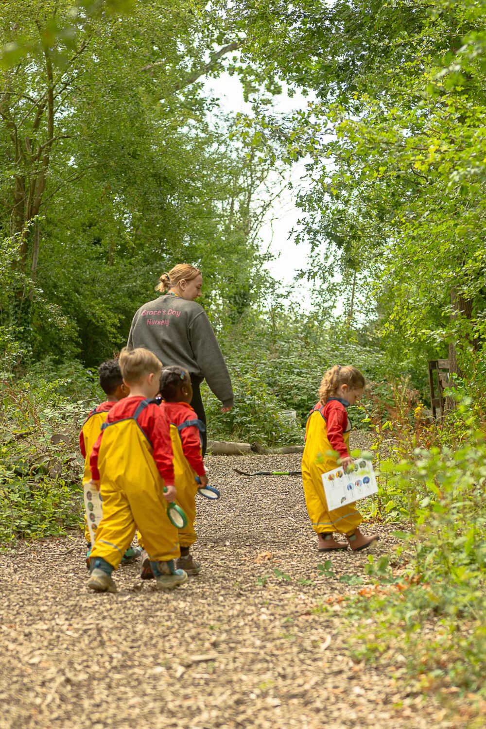 A member of staff exploring the woods with a group of children and their magnifying glasses