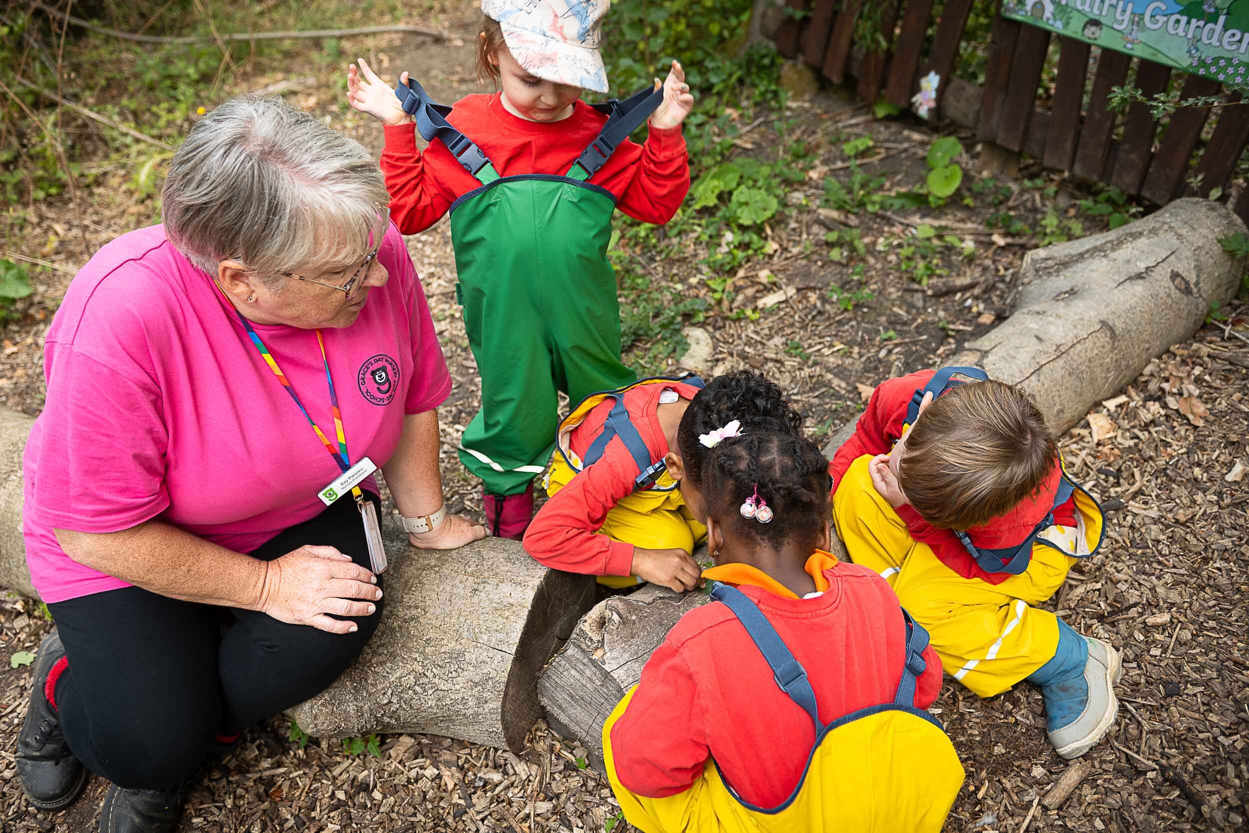 A member of staff watching over a group of children while they are looking at tree stumps