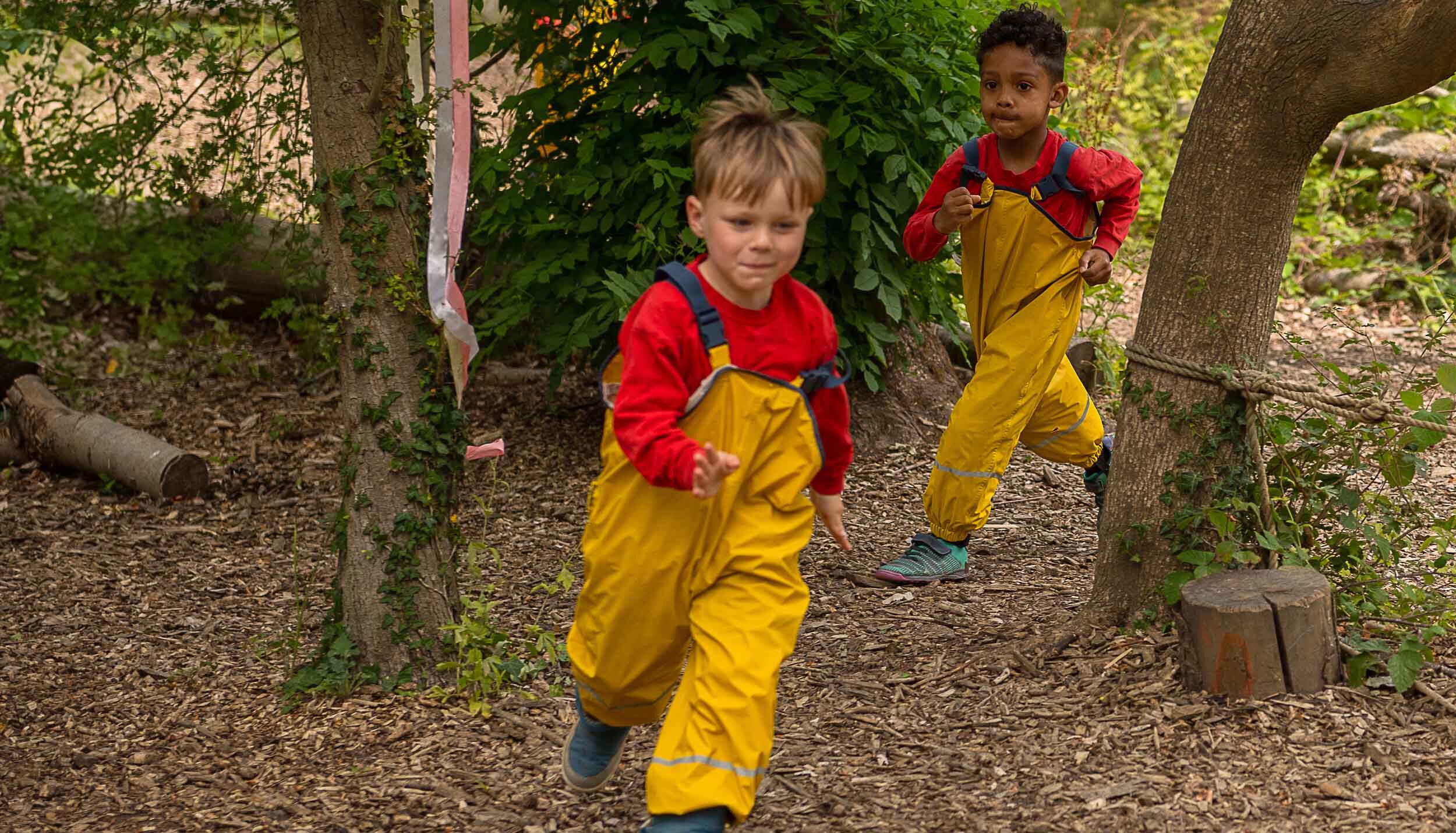 Two children running after each other through the woods