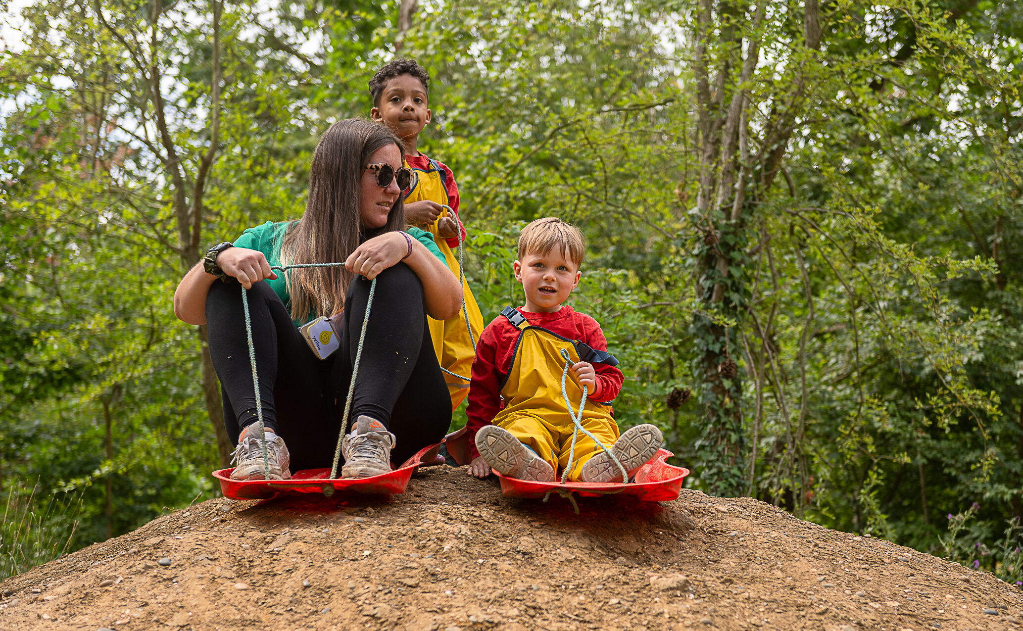 Nursery carer and children on sleighs on top of mud mountain