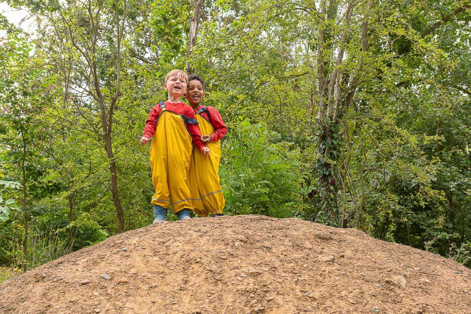 two boys smiling and laughing on top of a dirt mound