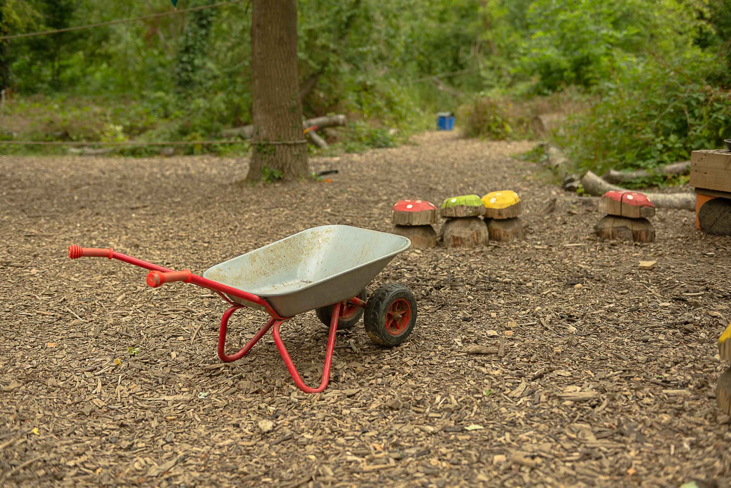 A wheelbarrow and carved wooden mushrooms in the forest school