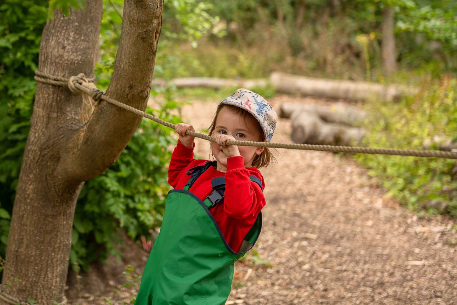 A little girl holding on to a rope to balance, peering over the top of her hands